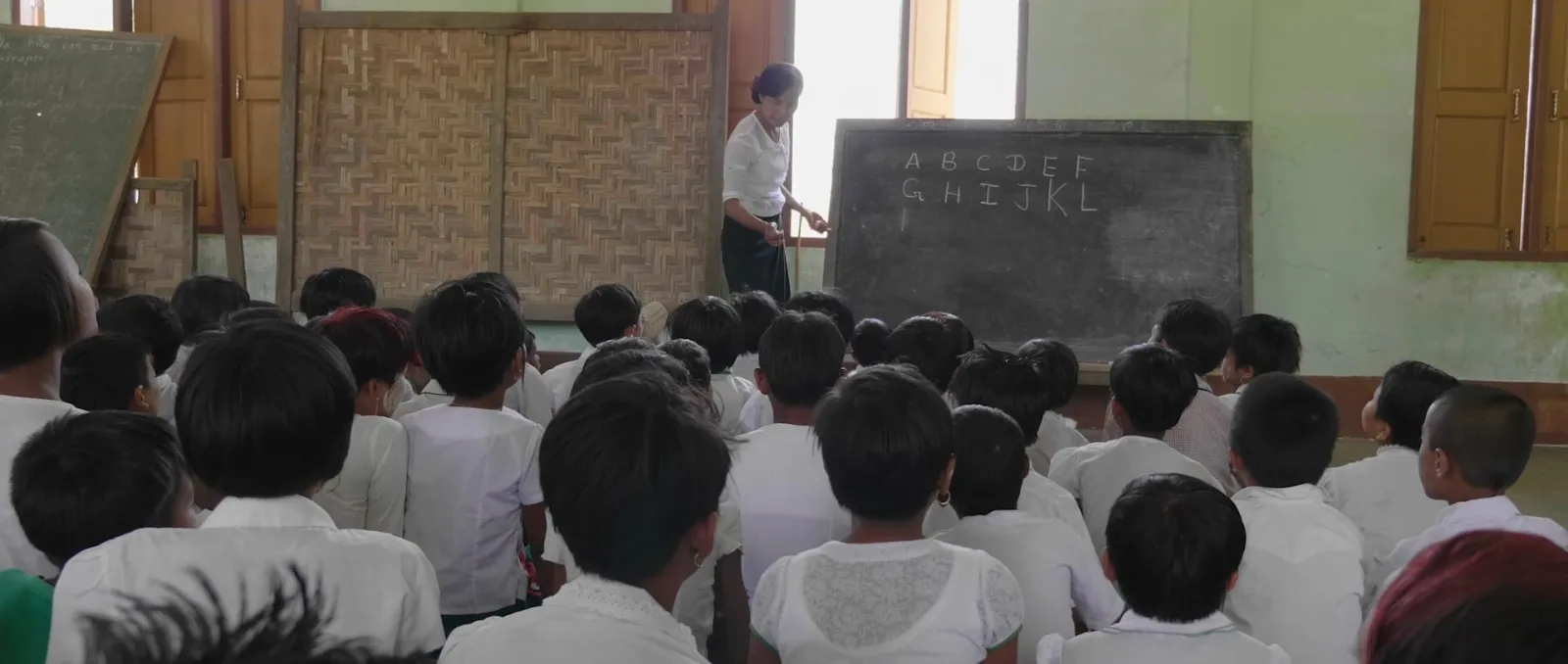 A teacher at a blackboard in front of a full classroom of students