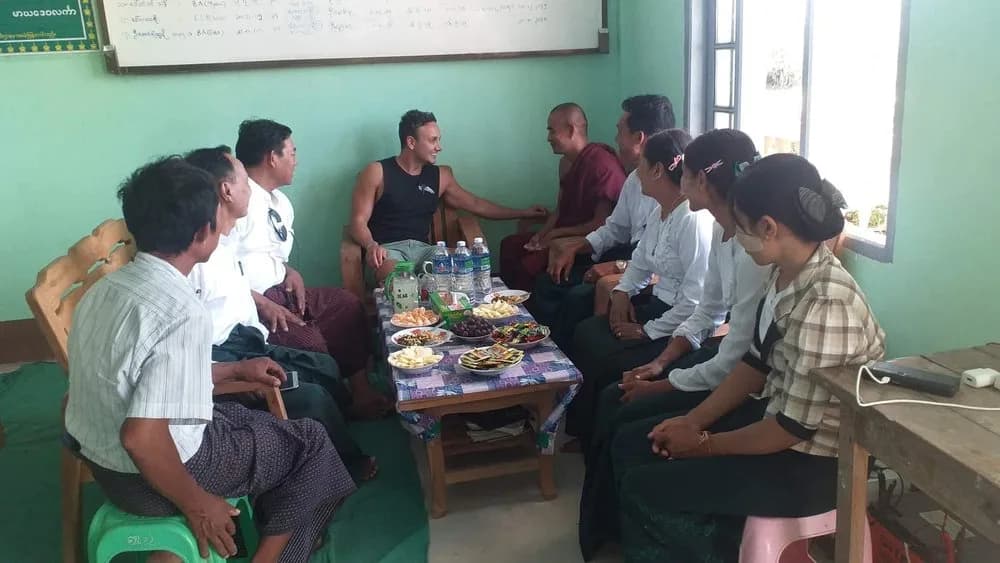 A visitor talking with local people around a low table in a classroom