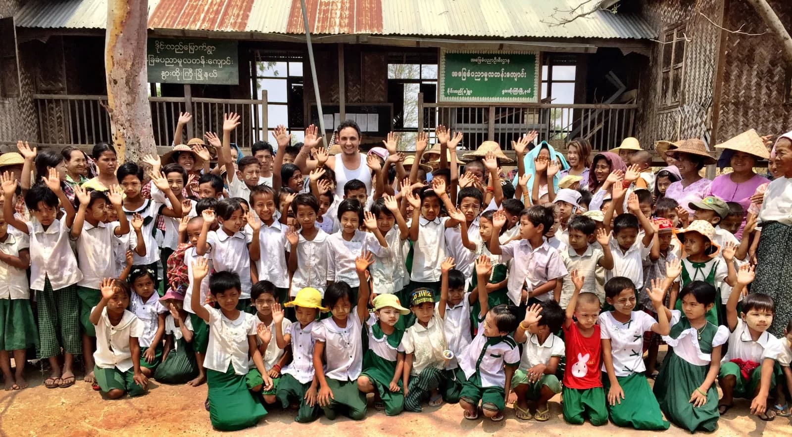 A large crowd of students in uniform waving in front of a school with a green sign