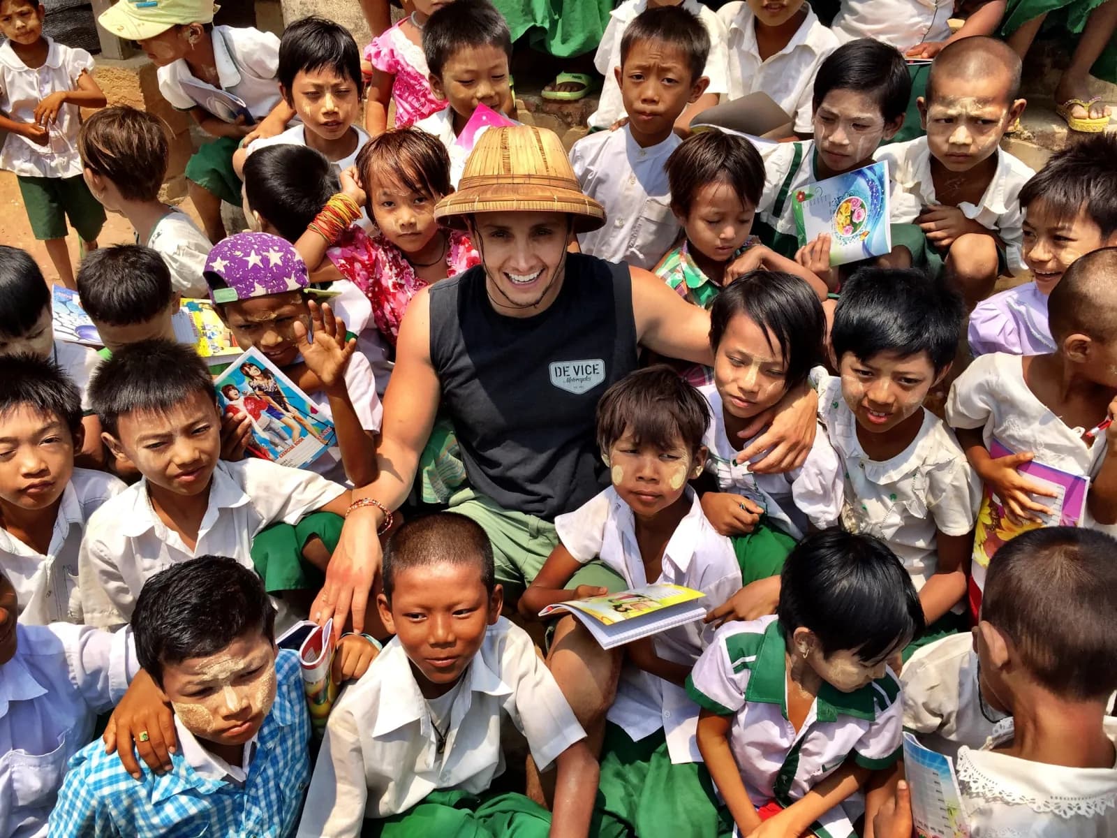 A visitor in a straw hat sitting among schoolchildren, some holding up books